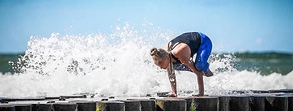 Patrycja Adaszewska ćwiczy jogę na plaży z widokiem na morze i rozbrysk fal w tle.