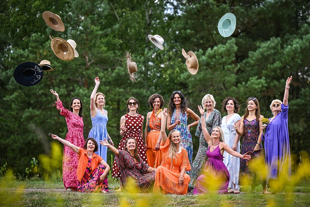 Grupa kobiet w kolorowych sukienkach rzuca kapelusze w górę podczas wyjazdu Kobieta w Pełni.