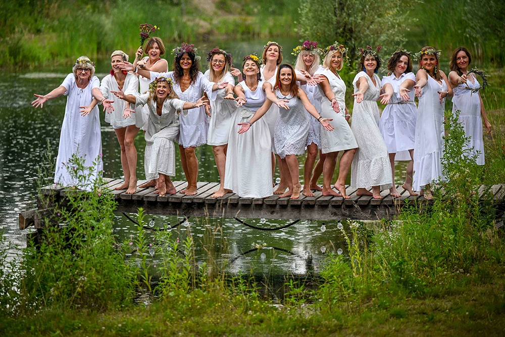 Kobiety ubrane na biało z wiankami na głowach stoją na pomoście nad wodą podczas weekendu kobiecości.